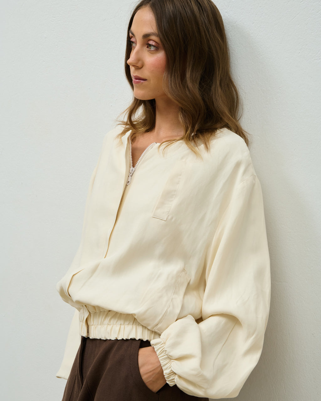 Model wearing the beige Krys Bomber jacket over brown trousers, side view