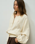 Model wearing the beige Krys Bomber jacket over brown trousers, side view
