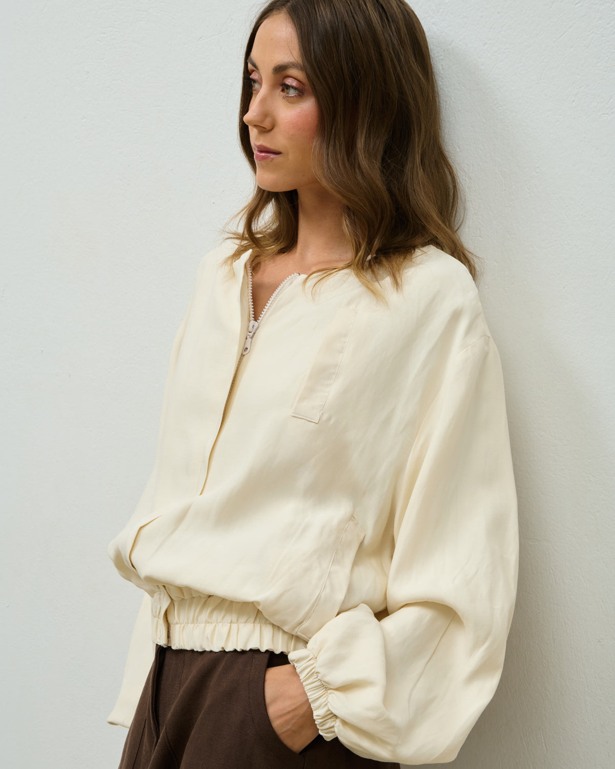 Model wearing the beige Krys Bomber jacket over brown trousers, side view