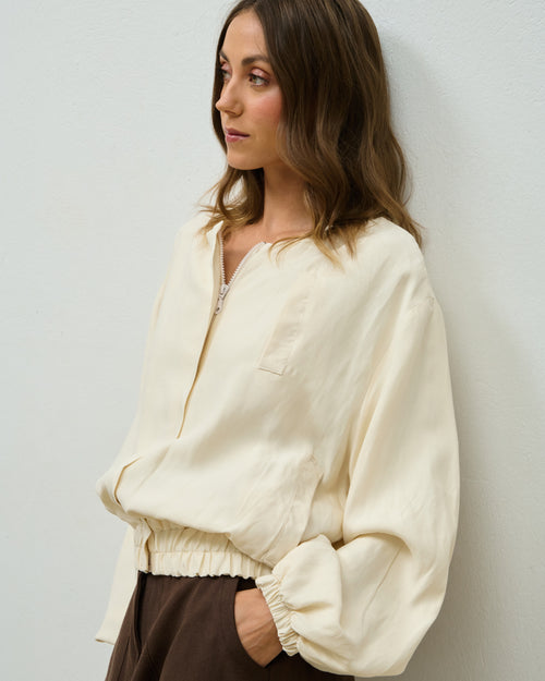 Model wearing the beige Krys Bomber jacket over brown trousers, side view
